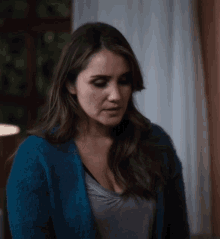 a woman wearing a blue sweater and a grey shirt looks down