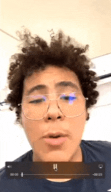 a man with curly hair and glasses is talking on a video call .