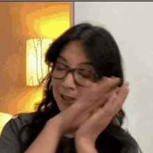 a woman wearing glasses is making a funny face while covering her face with her hands .