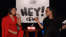 two people sit in front of a sign that says hey