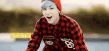 a young man with blue hair and a red hat is wearing a plaid shirt and a red beanie .