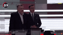 two men standing in front of a podium with the number 09 on it