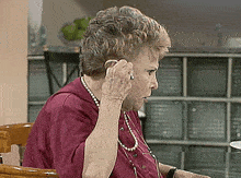 an elderly woman wearing a red shirt and pearls is talking on a cell phone
