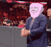 a man in a suit with a pink face is clapping in front of a raw sign