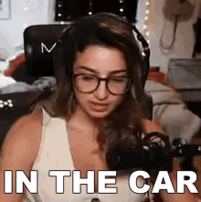 a woman wearing glasses and headphones is sitting in front of a microphone with the words in the car above her .