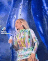 a woman in a colorful dress is dancing on a stage with a microphone in her hand .