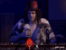 a man in a fur coat is standing in front of a microphone and saying `` i 'm ok '' .