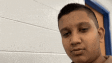 a young boy with a shaved head is standing in front of a white brick wall and a blue door .