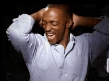 a man in a blue shirt is smiling with his hands behind his head