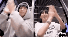 two young men are sitting next to each other on a ferris wheel and clapping their hands .