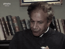 a man sitting in front of a bookshelf with globoplay written on the bottom right