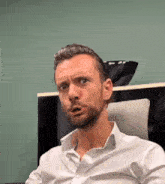 a man with a beard wearing a white shirt is making a funny face