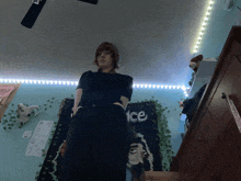a woman in a black dress stands in front of a tapestry that says ice on it