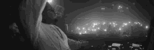 a black and white photo of a man playing a dj set in front of a crowd .