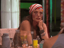 a woman wearing sunglasses and a head scarf sits at a table with bottles