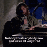 a man with a beard sits at a table with the words nobody trusts anybody now