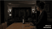 a woman is sitting at a table with a glass of wine and a bottle of wine