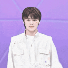 a young man wearing a white jacket and a white shirt is standing in front of a purple background