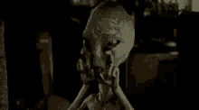 a close up of a statue of an alien in a dark room covering its face with its hands .