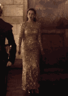 a woman in a long gold dress is standing in front of a wall