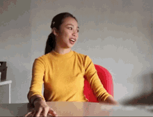 a woman in a yellow sweater sits at a desk