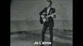 a black and white photo of a man playing a guitar with the words je l' aime in the bottom right corner