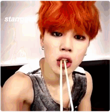 a young boy with red hair is eating noodles with chopsticks .