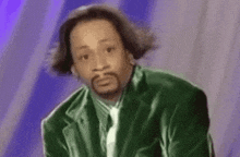 a man with a beard is wearing a green suit and tie and making a funny face .