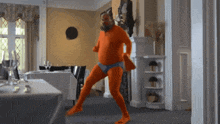 a man in an orange suit is dancing in a room