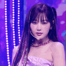 a woman wearing a purple dress and a necklace is standing in front of purple lights