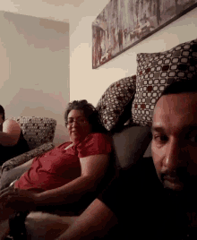 a woman in a red shirt sits on a couch next to a man with a beard