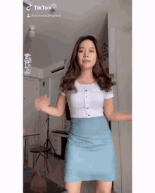 a woman in a white shirt and blue skirt is dancing in a room .