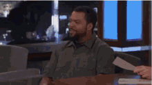 a man with a beard is sitting at a table with a piece of paper in front of him .