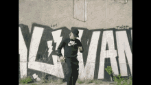 a man in a nike sweatshirt is standing in front of a wall that has graffiti on it .