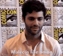 a man with a beard is standing in front of a comic con wall .