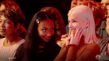 a group of people are sitting in a theatre watching a show and one woman is covering her mouth with her hand .