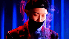 a man wearing a beret and a mask is standing in front of a blue curtain .