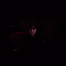 a woman is sitting in a dark room with a red light behind her
