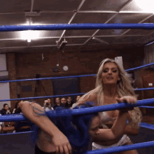a woman with blue hair is hugging another woman in a boxing ring