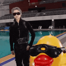 a man in a black suit is standing next to a yellow rubber duck