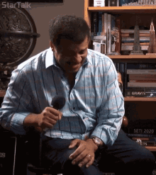 a man is sitting in front of a bookshelf with a book titled gravity