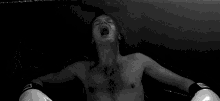 a black and white photo of a shirtless man wearing boxing gloves .