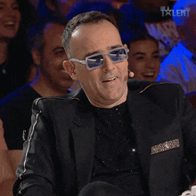 a man wearing sunglasses and a black suit is sitting in front of a crowd with the word talent on the bottom