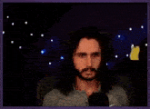 a man with long hair and a beard is sitting in front of a microphone in a dark room