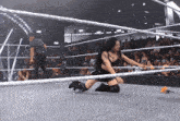 a woman is kneeling in a wrestling ring while a referee watches