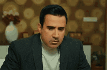 a man in a suit and turtleneck is making a funny face while sitting at a desk .