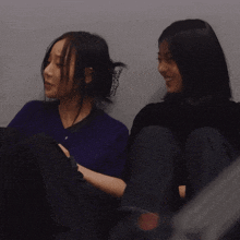 two women sitting next to each other with one wearing a purple sweater
