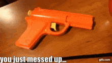 an orange toy gun is sitting on a wooden table with the words " you just messed up " written below it