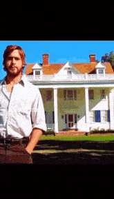 a man stands in front of a large white house with his hands in his pockets