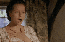 a woman with a surprised look on her face holds her hand to her chest